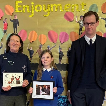 Tom Randall MP with the Killisick Junior School Headteacher holding the winning entry designed by Annabelle and Annabelle aged 10 with a framed and signed photo of the PM with her design.